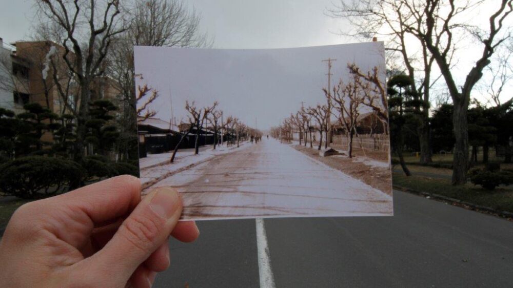 Im Hintergrund eine Straße mit Landschaft an beiden Seiten, die von einem hochgehaltenen Foto von der selben Straße im Vordergrund verdeckt wird