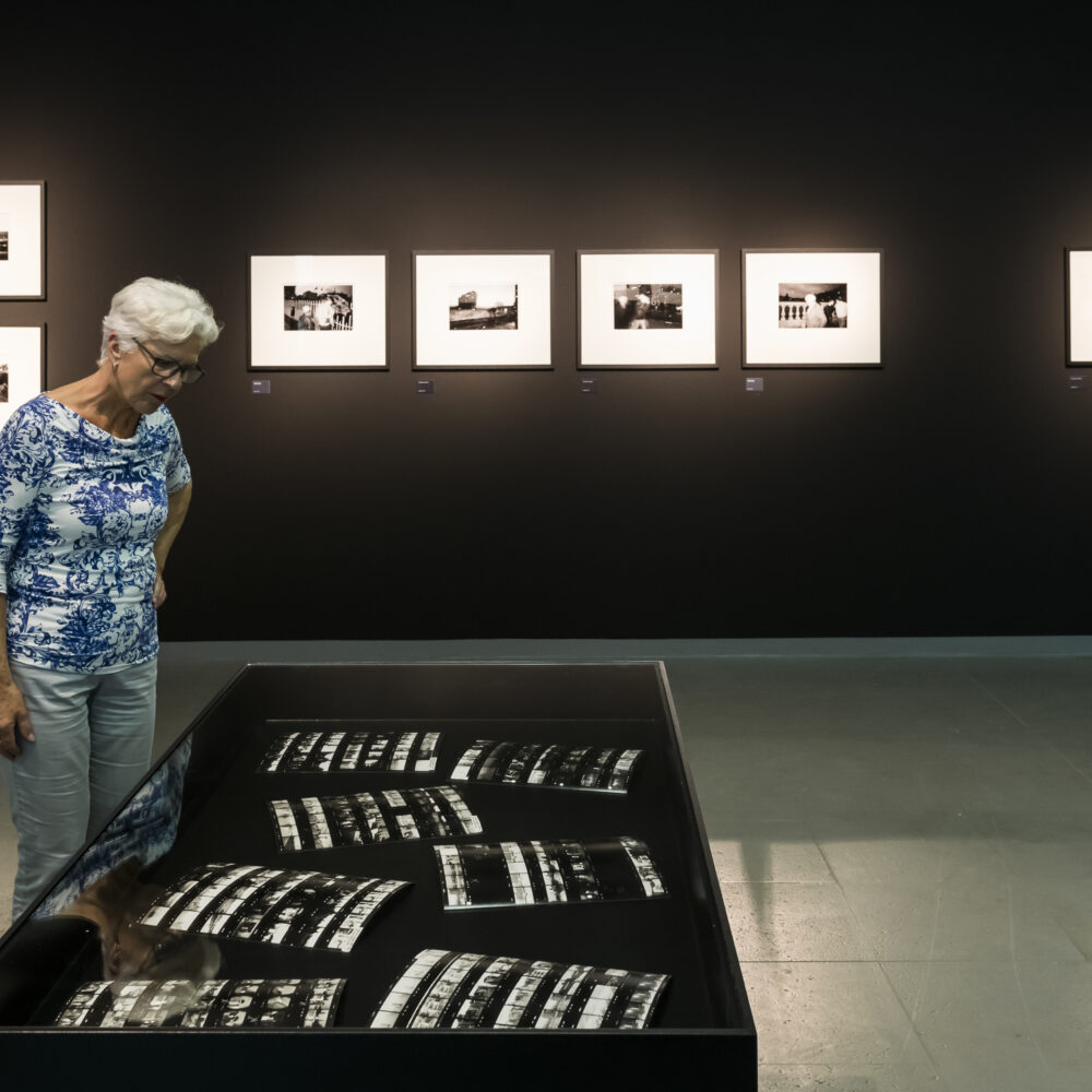 Eine Frau schaut in der Martin Parr Retrospektive in eine Vitrine